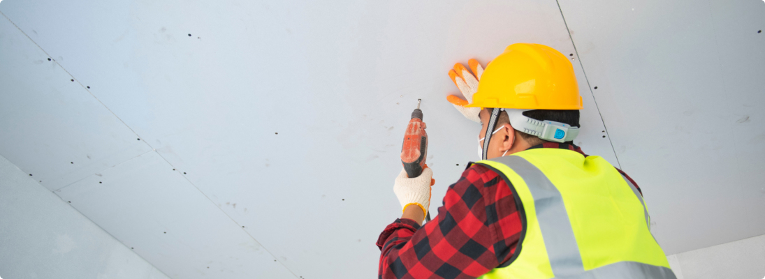 Construction worker assemble a suspended ceiling with drywall and fixing the drywall to the ceiling metal frame with screwdriver. Renovation, construction and ceiling installation concept.