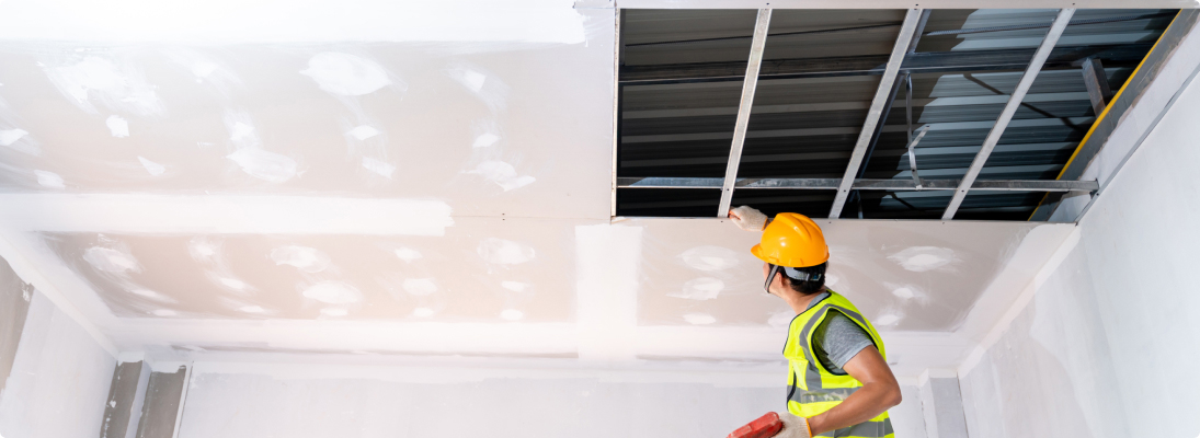 Construction worker assemble a suspended ceiling with drywall and fixing the drywall to the ceiling metal frame with screwdriver. Renovation, construction and ceiling installation concept.