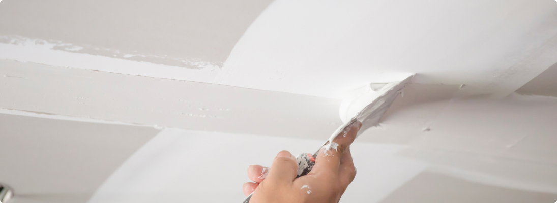 Construction worker assemble a suspended ceiling with drywall and fixing the drywall to the ceiling metal frame with screwdriver. Renovation, construction and ceiling installation concept.