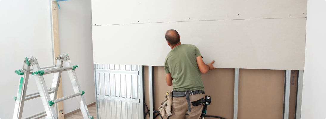 Construction worker assemble a suspended ceiling with drywall and fixing the drywall to the ceiling metal frame with screwdriver. Renovation, construction and ceiling installation concept.