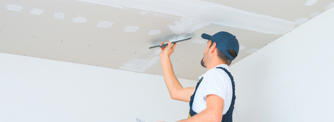 Construction worker assemble a suspended ceiling with drywall and fixing the drywall to the ceiling metal frame with screwdriver. Renovation, construction and ceiling installation concept.