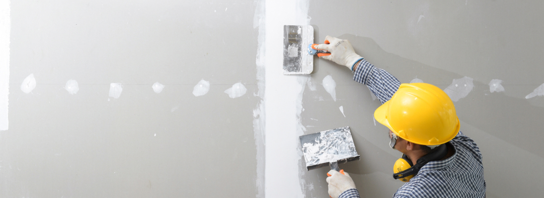 Construction worker assemble a suspended ceiling with drywall and fixing the drywall to the ceiling metal frame with screwdriver. Renovation, construction and ceiling installation concept.