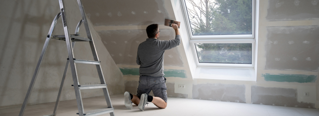 Construction worker assemble a suspended ceiling with drywall and fixing the drywall to the ceiling metal frame with screwdriver. Renovation, construction and ceiling installation concept.