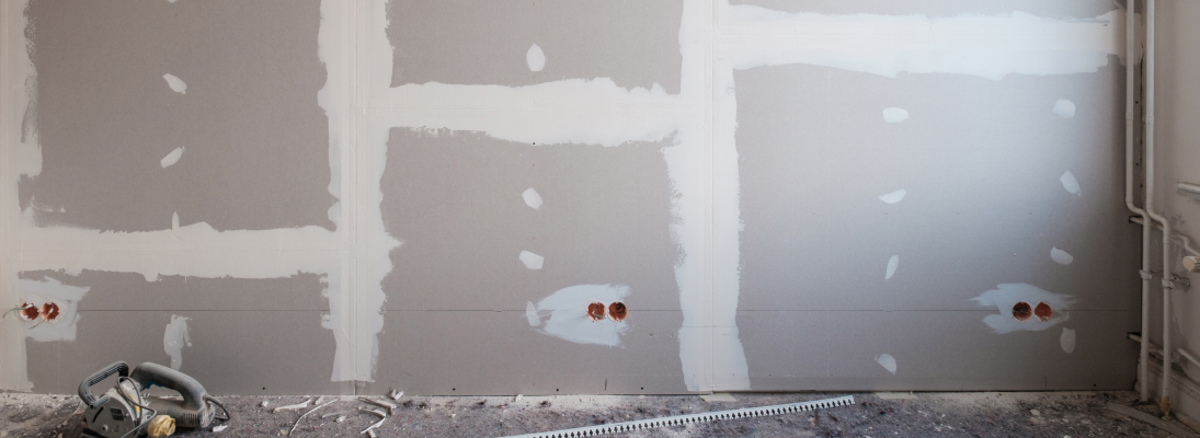 Construction worker assemble a suspended ceiling with drywall and fixing the drywall to the ceiling metal frame with screwdriver. Renovation, construction and ceiling installation concept.