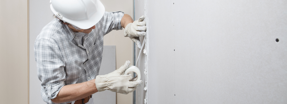 Construction worker assemble a suspended ceiling with drywall and fixing the drywall to the ceiling metal frame with screwdriver. Renovation, construction and ceiling installation concept.