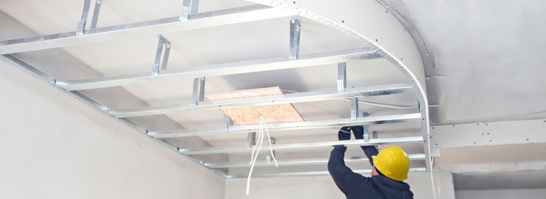 Construction worker assemble a suspended ceiling with drywall and fixing the drywall to the ceiling metal frame with screwdriver. Renovation, construction and ceiling installation concept.