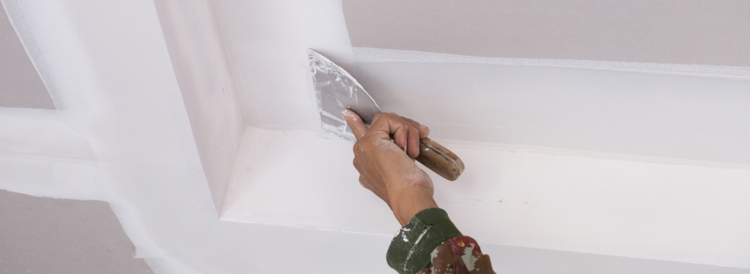 Construction worker assemble a suspended ceiling with drywall and fixing the drywall to the ceiling metal frame with screwdriver. Renovation, construction and ceiling installation concept.