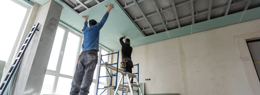 Construction worker assemble a suspended ceiling with drywall and fixing the drywall to the ceiling metal frame with screwdriver. Renovation, construction and ceiling installation concept.