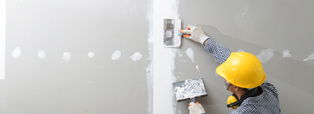 Construction worker assemble a suspended ceiling with drywall and fixing the drywall to the ceiling metal frame with screwdriver. Renovation, construction and ceiling installation concept.