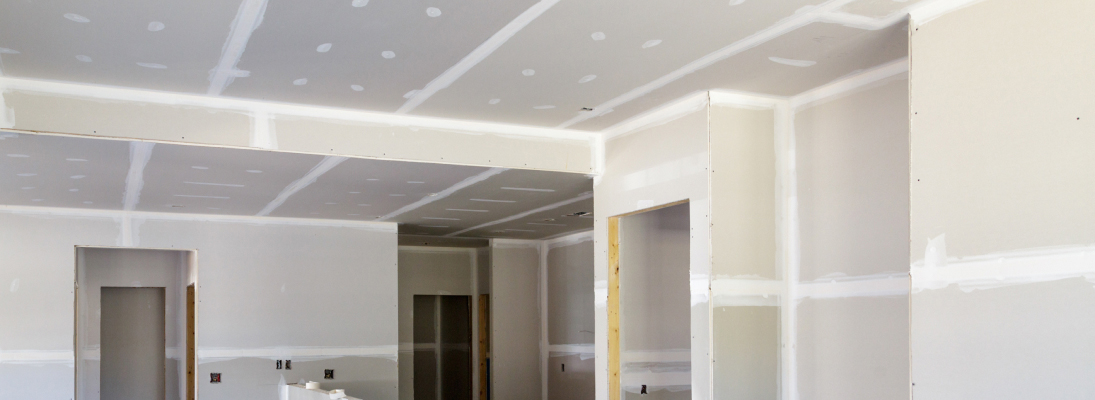 Construction worker assemble a suspended ceiling with drywall and fixing the drywall to the ceiling metal frame with screwdriver. Renovation, construction and ceiling installation concept.