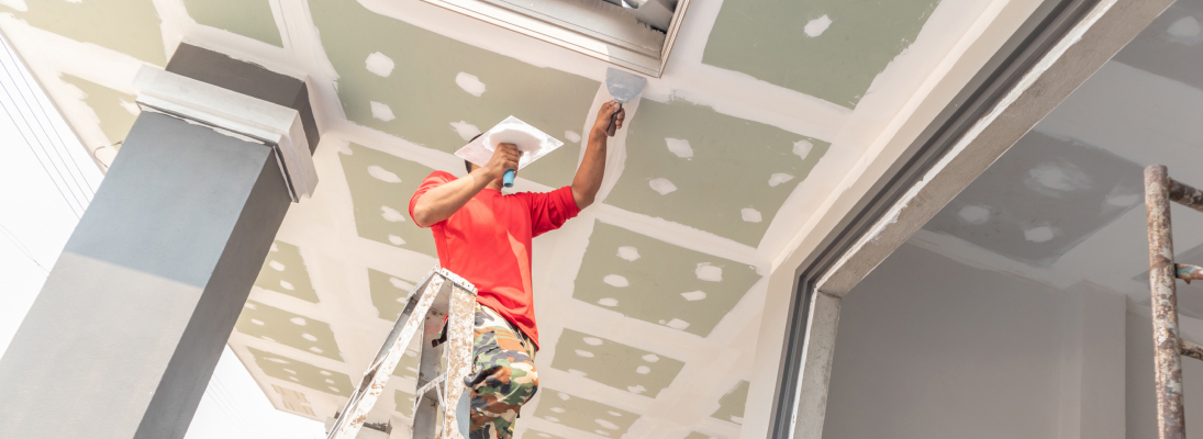 Construction worker assemble a suspended ceiling with drywall and fixing the drywall to the ceiling metal frame with screwdriver. Renovation, construction and ceiling installation concept.