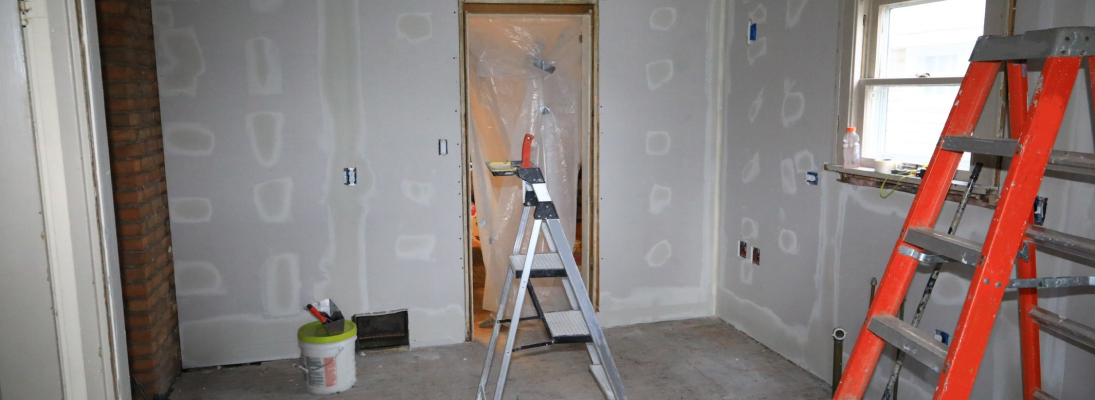 Construction worker assemble a suspended ceiling with drywall and fixing the drywall to the ceiling metal frame with screwdriver. Renovation, construction and ceiling installation concept.