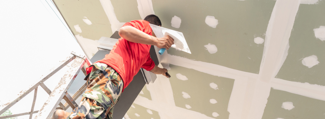 Construction worker assemble a suspended ceiling with drywall and fixing the drywall to the ceiling metal frame with screwdriver. Renovation, construction and ceiling installation concept.