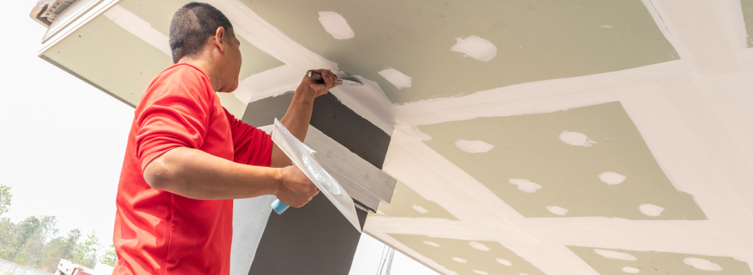 Construction worker assemble a suspended ceiling with drywall and fixing the drywall to the ceiling metal frame with screwdriver. Renovation, construction and ceiling installation concept.